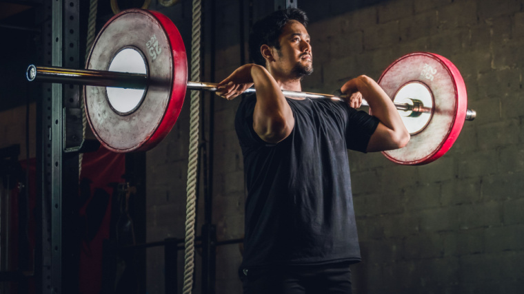 Person in dark hold holding barbell on shoulders