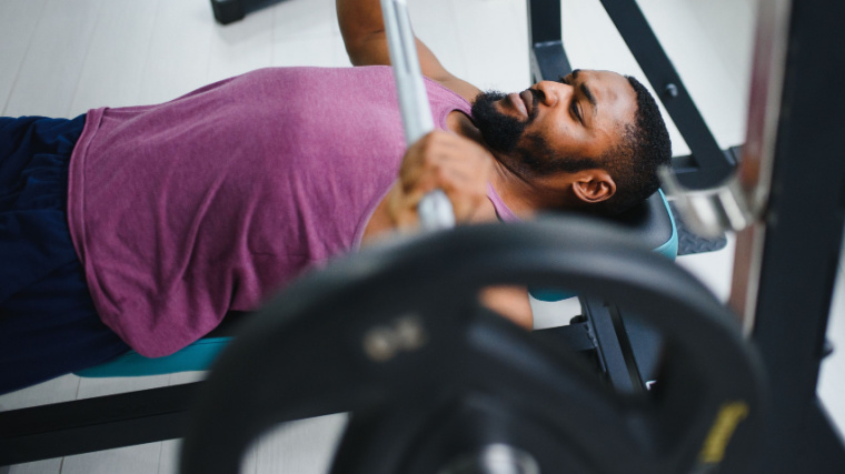 person in gym lower barbell in bench press