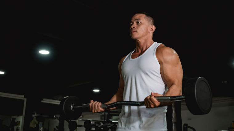 muscular person in gym curling barbell