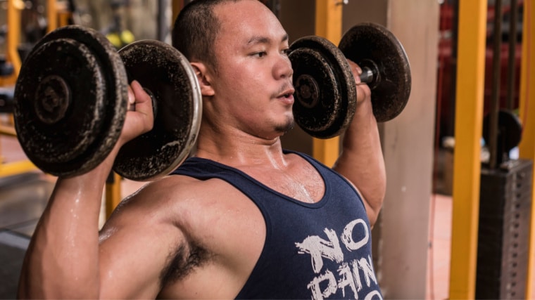 muscular person in gym pressing dumbbells