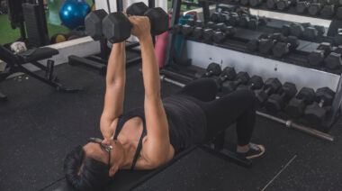 person in gym locking out dumbbell press