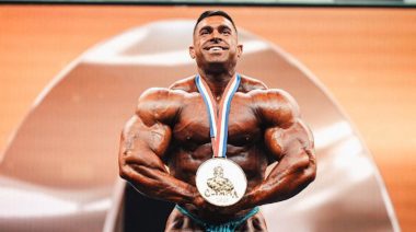 Derek Lunsford stands on stage with the first-place medal for winning the 2023 Mr. Olympia contest.