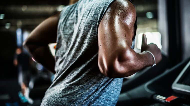 Muscular person sweating in gym while running on treadmill