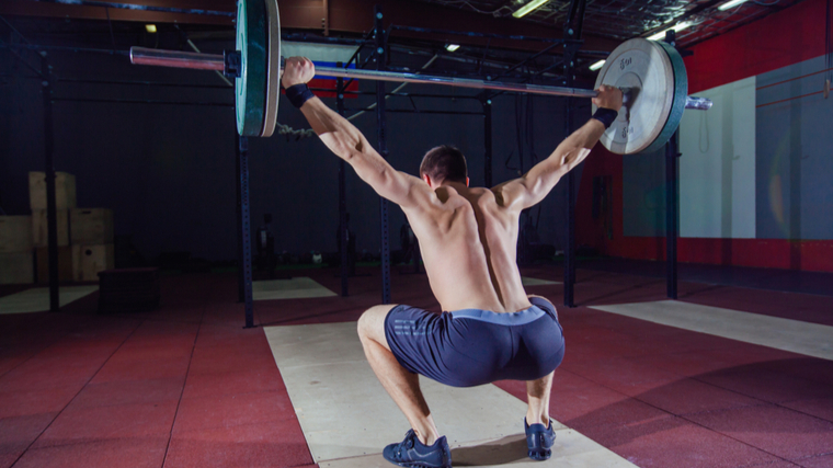 Muscular man performing squat with barbell overhead