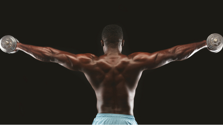 Man in dark room performing dumbbell shoulder exercise