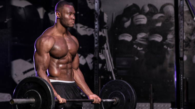 shirtless muscular person in gym curling barbell