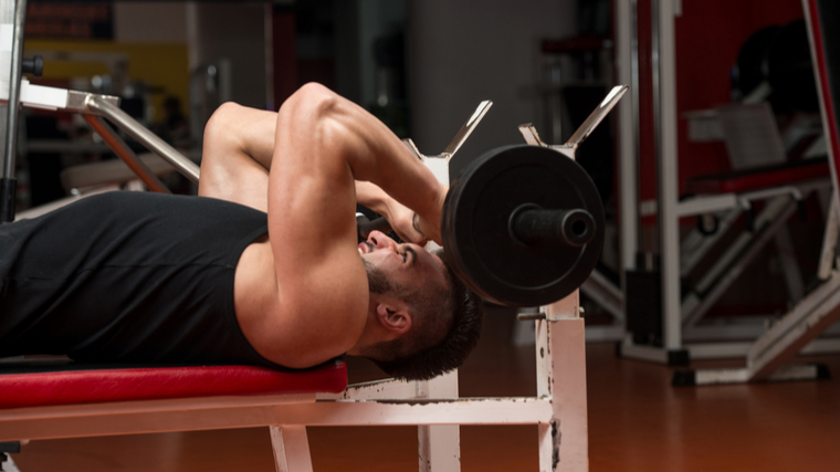 Man in gym performing triceps exercise with barbell