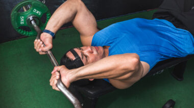 muscular person in gym performing barbell triceps exercise on flat bench