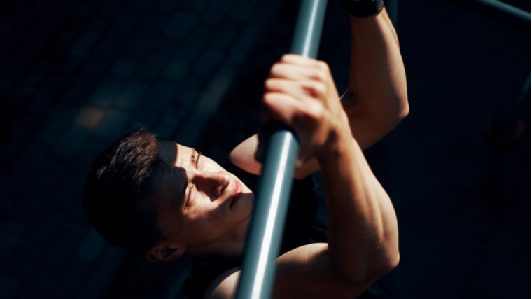 Person in dark gym reaching up grabbing bar