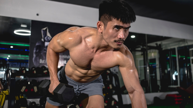 Muscular man performing dumbbell row exercise in gym